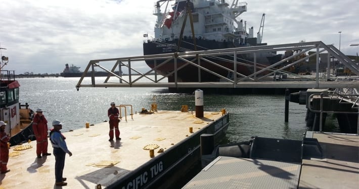 workers at a dock maneuvering a large metal structure with a crane near a boat