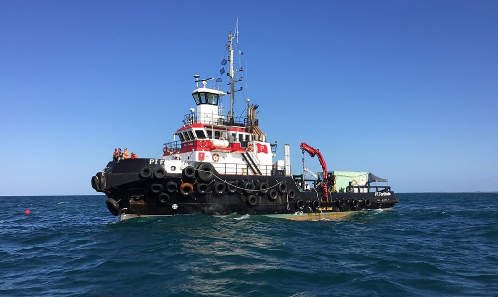 tugboat on blue ocean with crew visible on deck